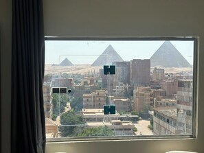 A window view of a cityscape with buildings and pyramids in the distance. - Vista Pyramids Boutique Hotel (Giza)