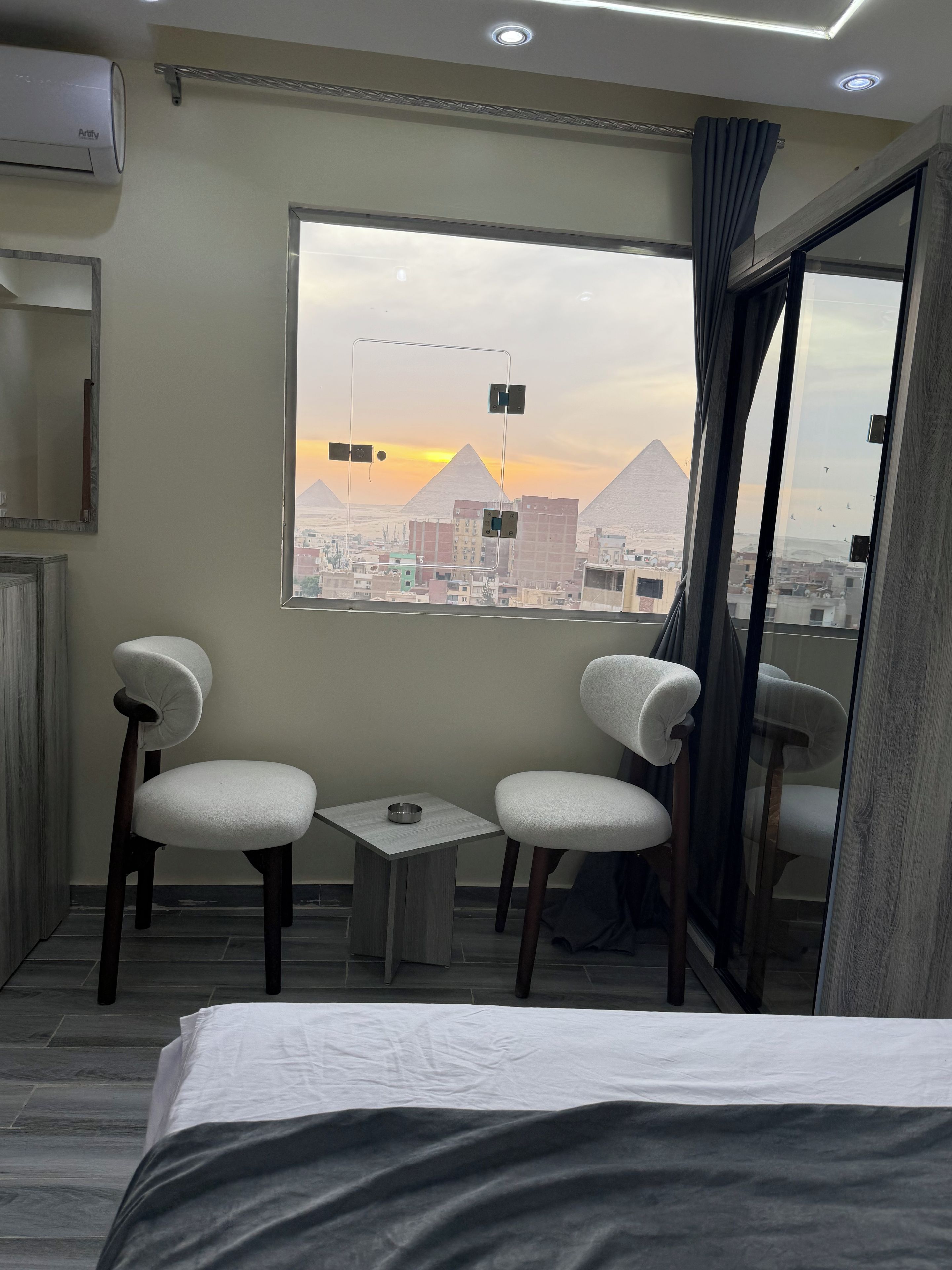 Een hotelkamer met een bed, twee stoelen, een klein tafeltje en een raam met uitzicht op piramides.
