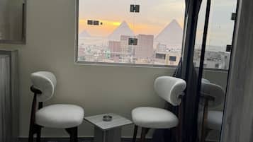 Een hotelkamer met een bed, twee stoelen, een klein tafeltje en een raam met uitzicht op piramides.