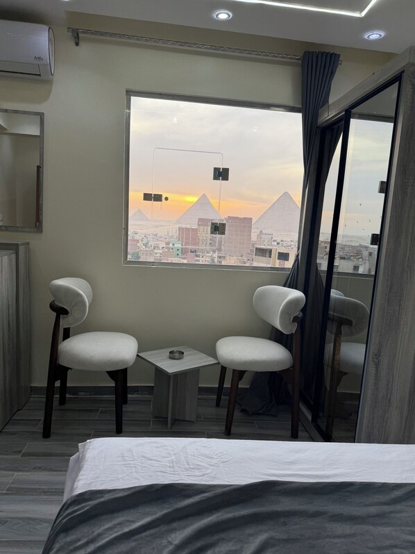 A hotel room with a bed, two chairs, a small table, and a window with a view of pyramids. - Vista Pyramids Boutique Hotel (Giza)