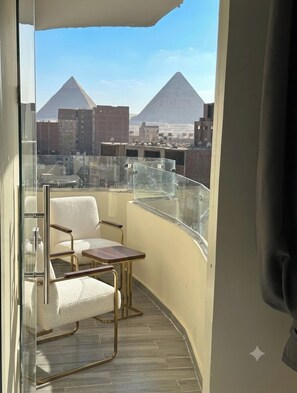 A balcony with a view of pyramids, a chair, and a small table. - Vista Pyramids Boutique Hotel (Giza)