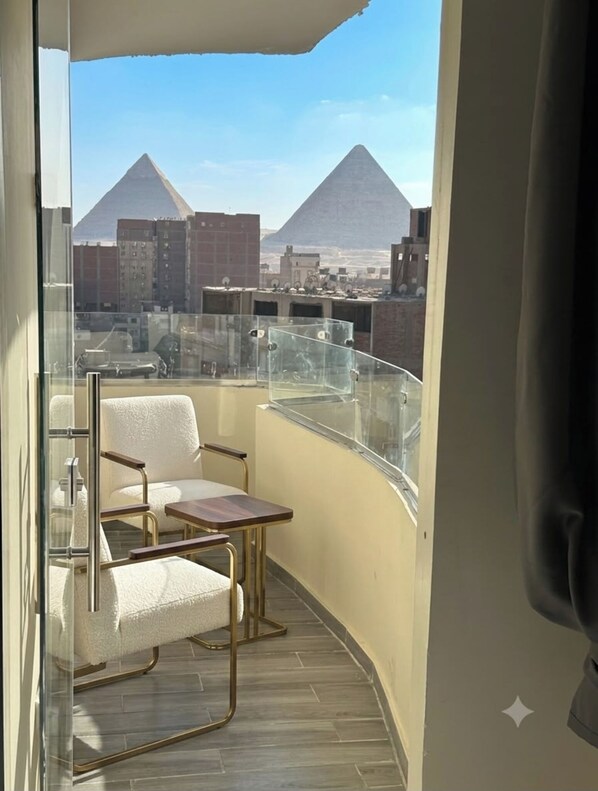 A balcony with a view of pyramids, a chair, and a small table. - Vista Pyramids Boutique Hotel (Giza)