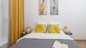 A neatly made bed with a book on it, two bedside lamps, and a window with curtains.