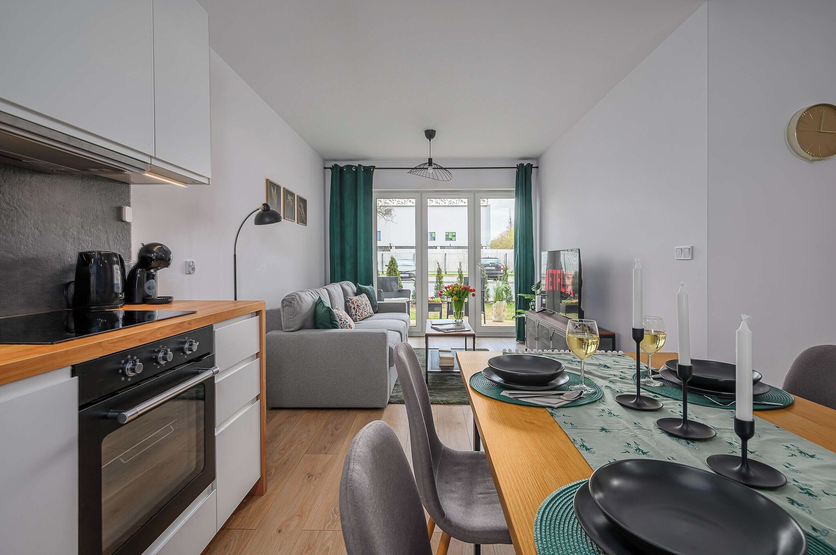 A modern kitchen with a dining area, a sofa, and a view through the window.