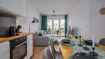 A modern kitchen with a dining area, a sofa, and a view through the window.