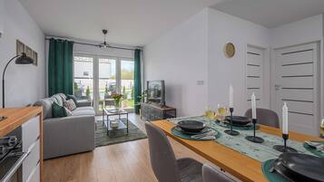 Een moderne woonkamer met een bank, een eettafel gedekt voor twee personen, een televisie en uitzicht door de glazen deur.