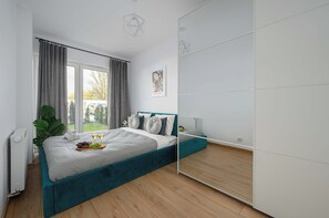 A bedroom with a bed, a large mirror, a window with curtains, and a plant. - Ground-floor Apartment Stay With Garden Terrace (Łódź)