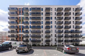 A multi-story residential building with balconies, a parking area, and two cars parked in front. - Ground-floor Apartment Stay With Garden Terrace (Łódź)