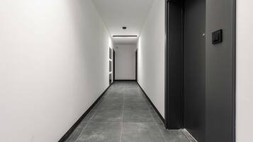 Een lange, smalle gang met een donkere deur aan de rechterkant en een lichtgekleurde wand aan de linkerkant.