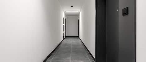A long, narrow hallway with a dark door on the right and a light-colored wall on the left.