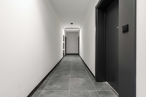 A long, narrow hallway with a dark door on the right and a light-colored wall on the left. - Ground-floor Apartment Stay With Garden Terrace (Łódź)
