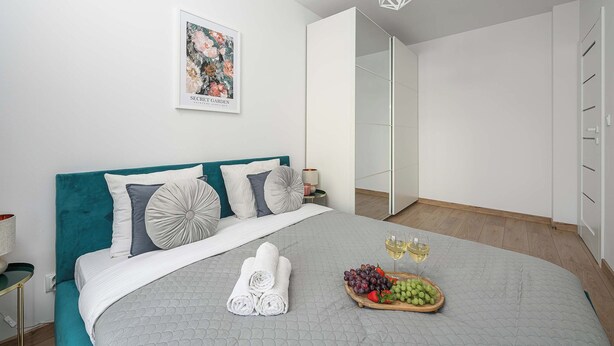 A modern bedroom with a bed, a bedside table, a mirror, and a wall-mounted artwork.