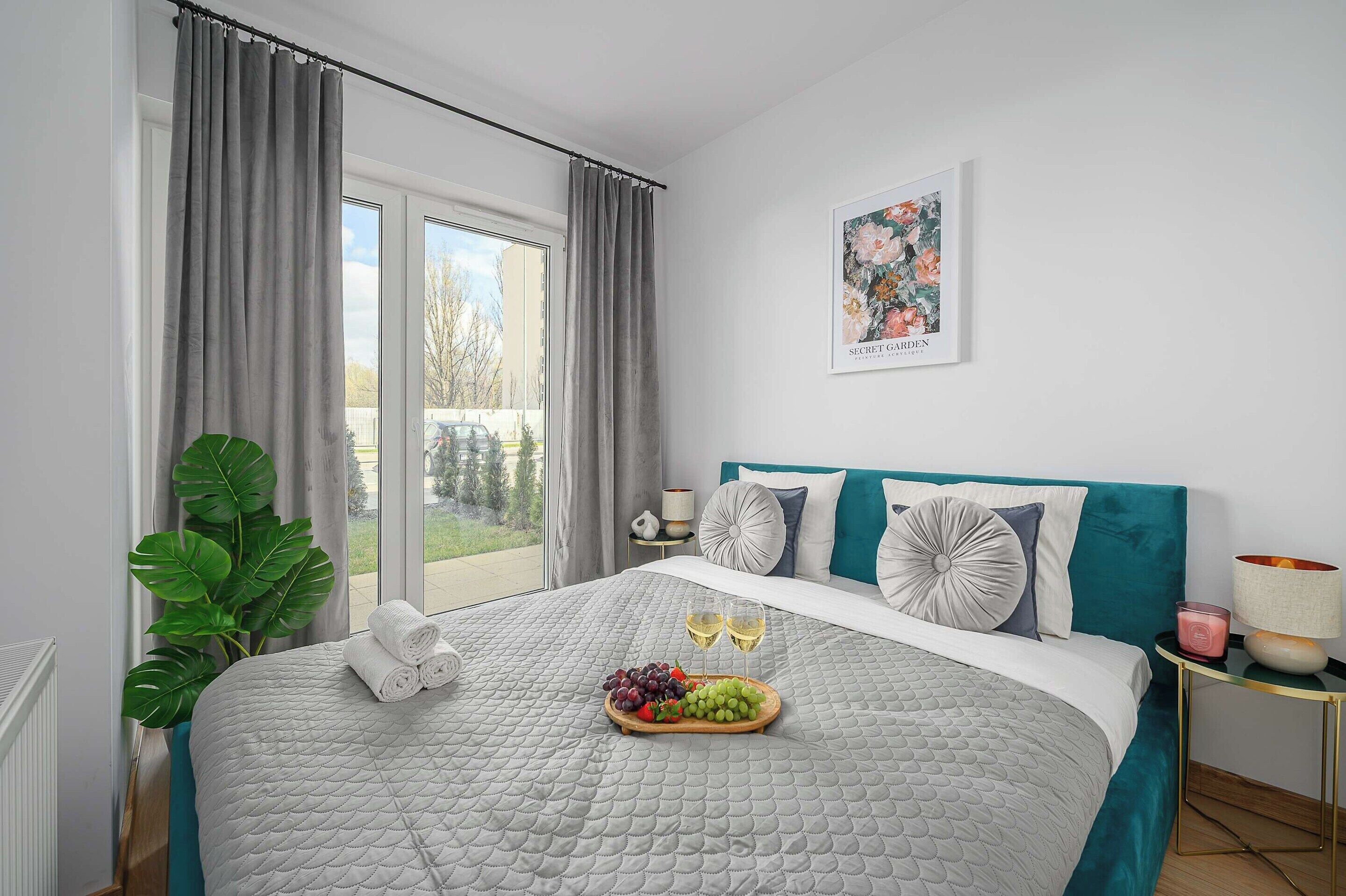 A bedroom with a bed, a window, a plant, and a painting on the wall.