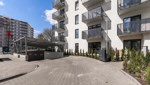 A modern apartment building with multiple balconies, a covered entrance, and a paved driveway.