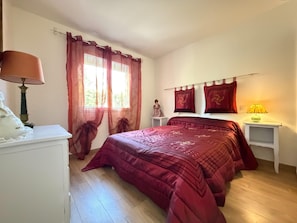 A bedroom with a bed, a nightstand, a lamp, and a window with curtains. - Charming Villa for 6 in Agde (Agde)