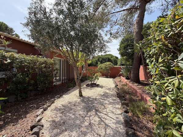 A gravel pathway leading to a building with a red exterior, surrounded by various shrubs and trees. - Charming Villa for 6 in Agde (Agde)