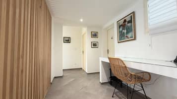 A modern office space with a glass desk, a wicker chair, and framed artwork on the wall.