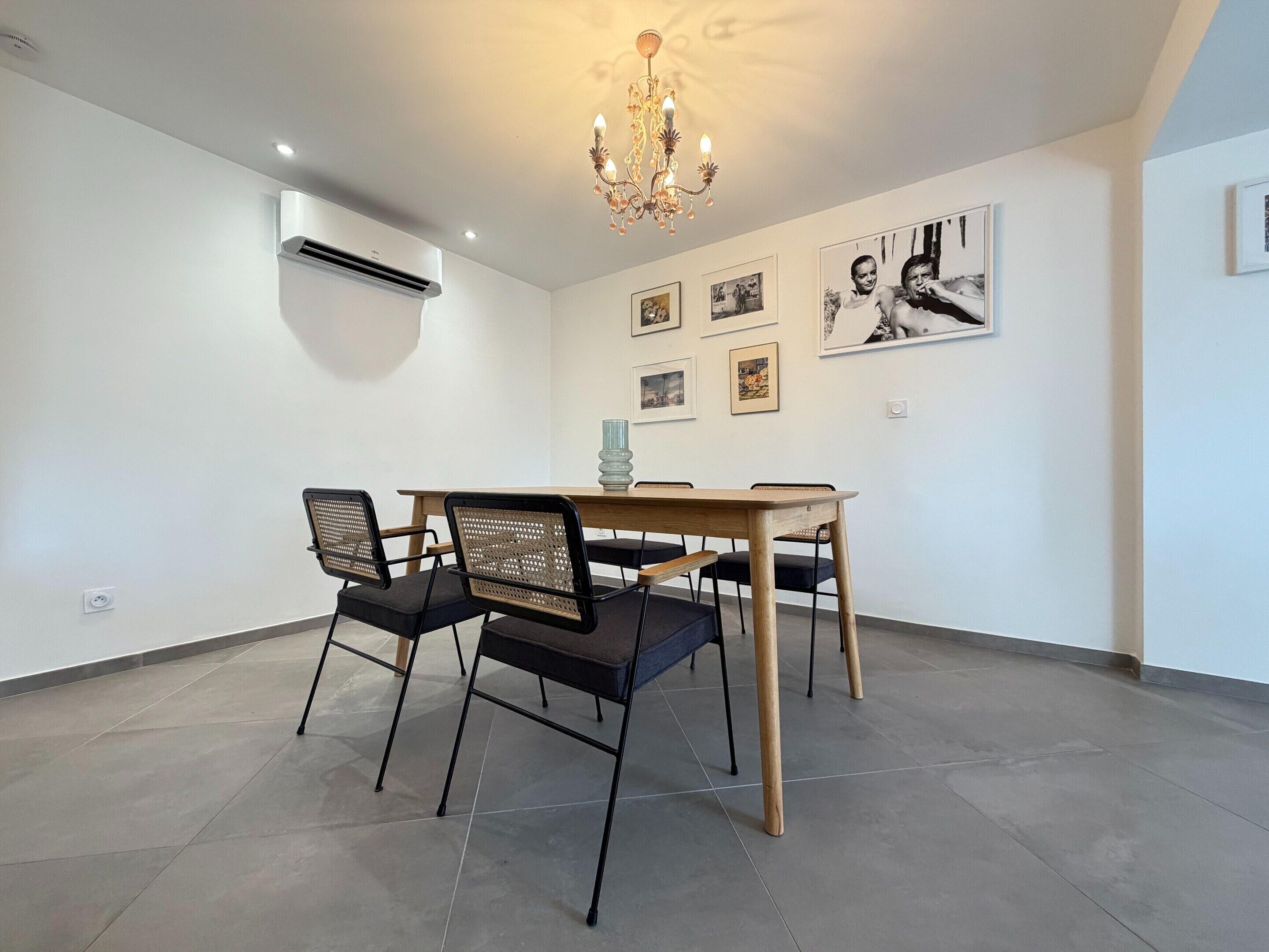 A dining area with a wooden table and chairs, a chandelier, and framed pictures on the wall.