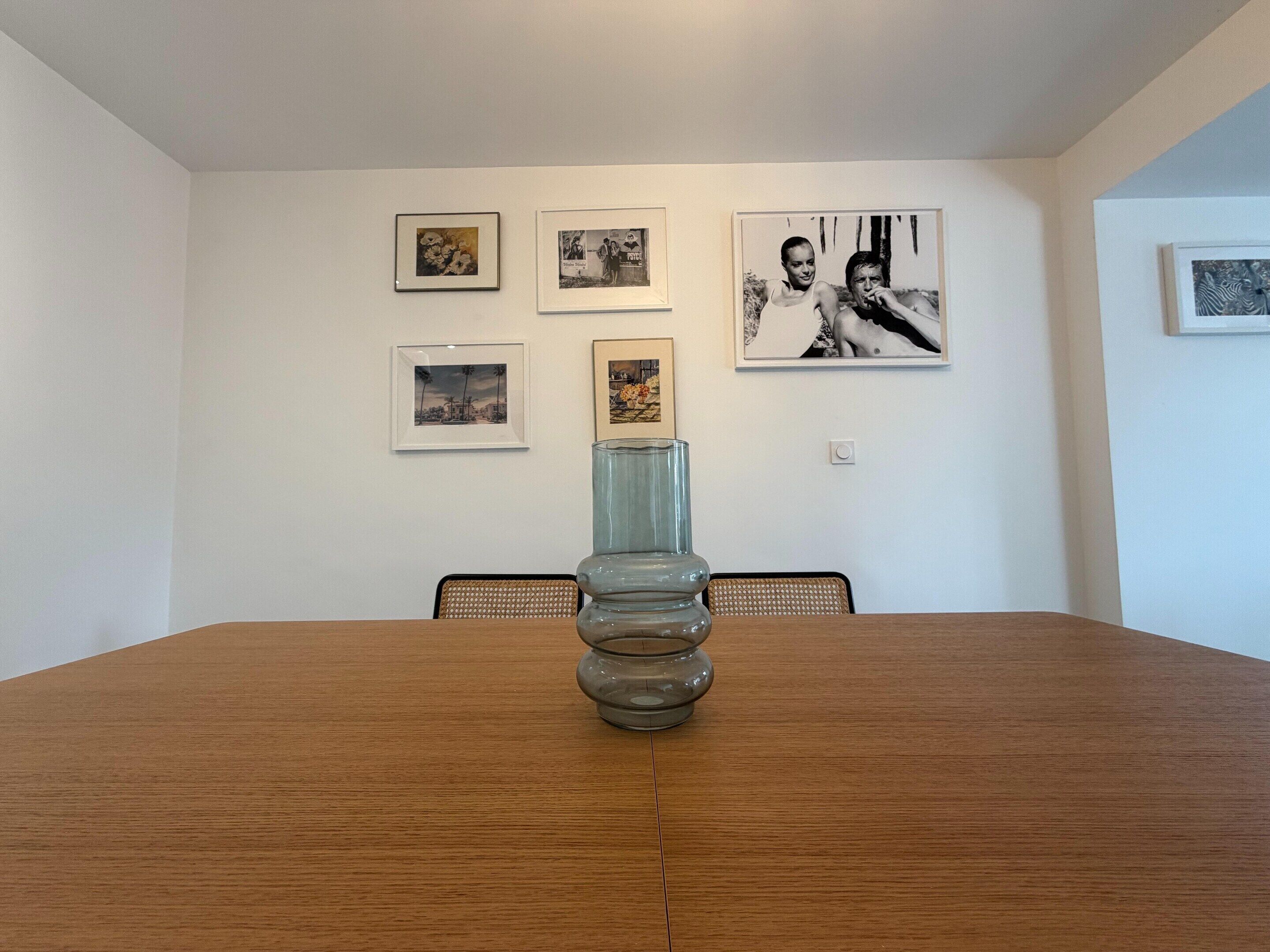 A dining table with a glass vase centerpiece, surrounded by chairs, in a room with white walls adorned with framed pictures.