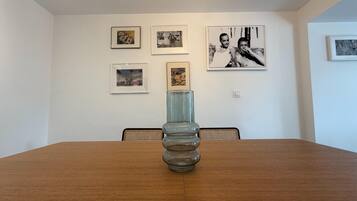 A dining table with a glass vase centerpiece, surrounded by chairs, in a room with white walls adorned with framed pictures.