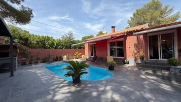 A residential property with a swimming pool, patio furniture, and a red building with large windows.