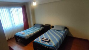Une chambre avec deux lits, une fenêtre avec des rideaux, une table de chevet et un luminaire fixé au mur.