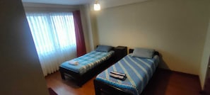 A room with two beds, a window with curtains, a bedside table, and a wall-mounted light fixture. - Spacious, comfortable 2-bedroom apartment, Sopocachi - La Paz, Bolivia (La Paz)