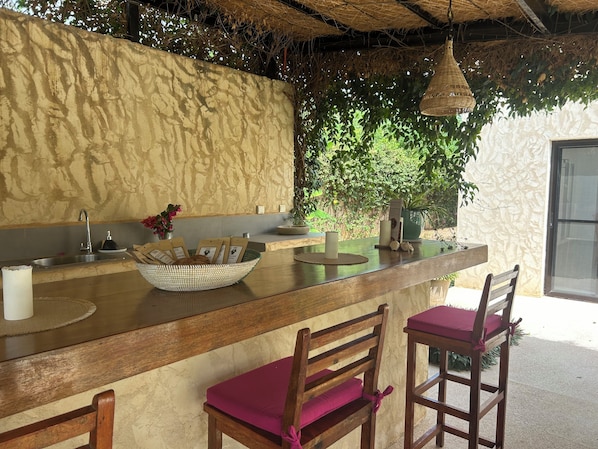A kitchen area with a stone wall, a wooden counter, a sink, and two bar stools with cushioned seats.