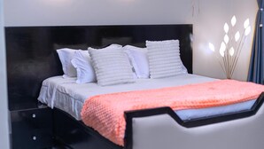 A bed with white bedding and a pink blanket, a black headboard, and a bedside table with drawers.