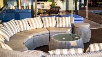 A sectional sofa with striped cushions, a round wicker ottoman, and a glass-top coffee table in a modern outdoor setting.
