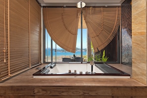 A modern bathroom with a large window, wooden blinds, and a view of the sea.