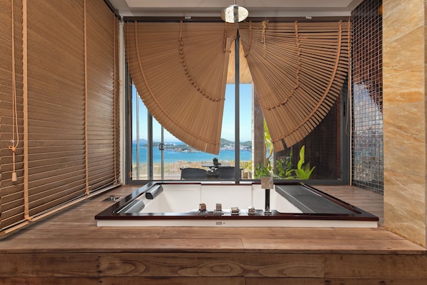 A modern bathroom with a large window, wooden blinds, and a view of the sea.