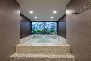 Área de spa com hidromassagem, escadas de acesso e vista para o verde lá fora.