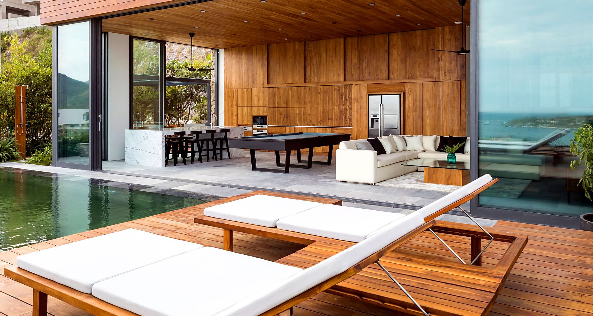 A modern outdoor living area with a pool, lounge chairs, a dining table, and a sofa.