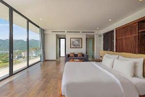 Une chambre d’hôtel moderne dotée d’un grand lit, d’un coin salon avec un canapé et offrant une vue sur les montagnes grâce à de grandes fenêtres du sol au plafond.