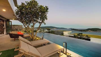 A rooftop infinity pool with lounge chairs, a tree, and a view of the coastline.