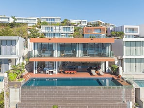 Una casa moderna de dos pisos con piscina en la azotea, zona de estar exterior y vistas a edificios vecinos.