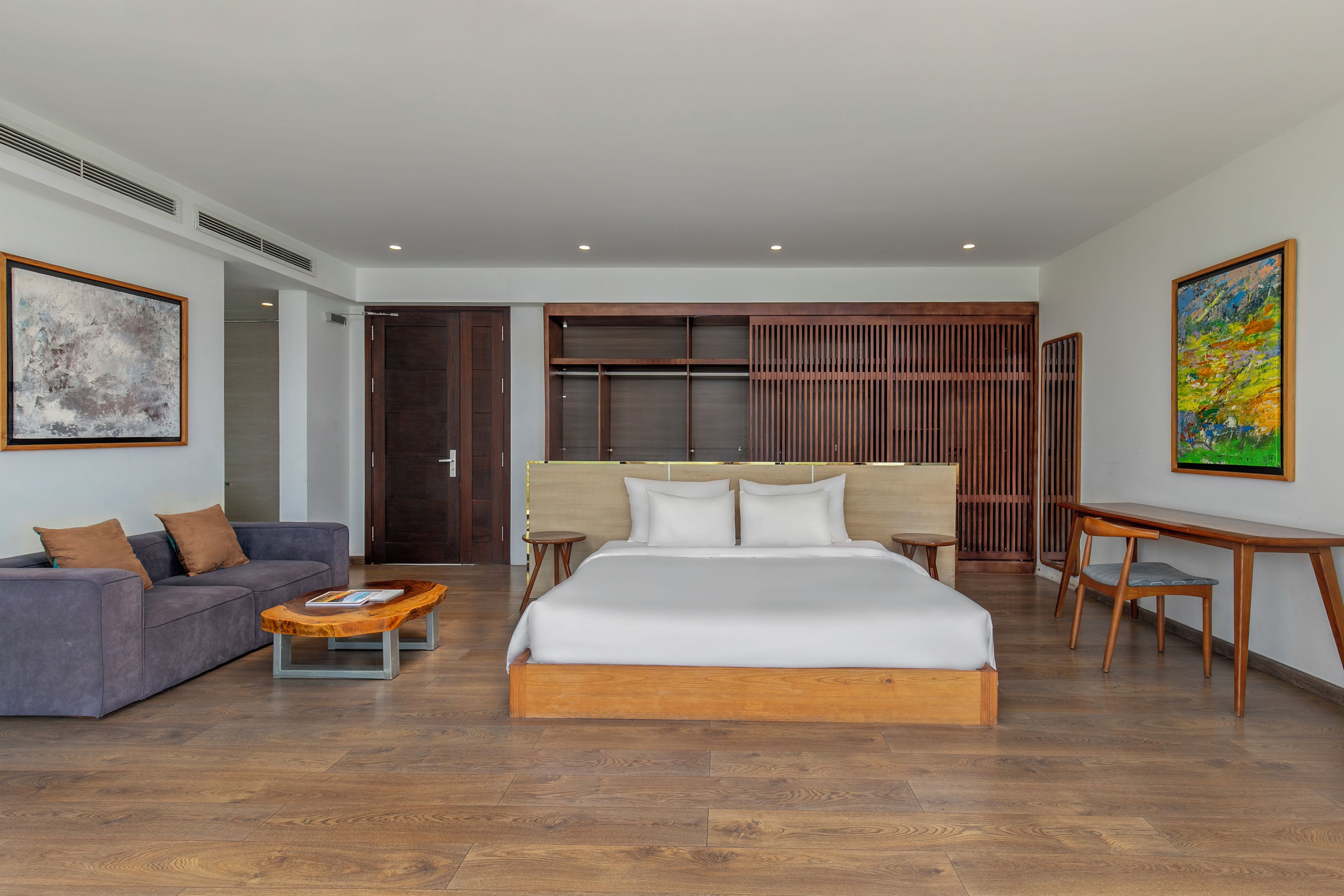 A modern hotel room with a large bed, a sofa, a small table, and a desk.