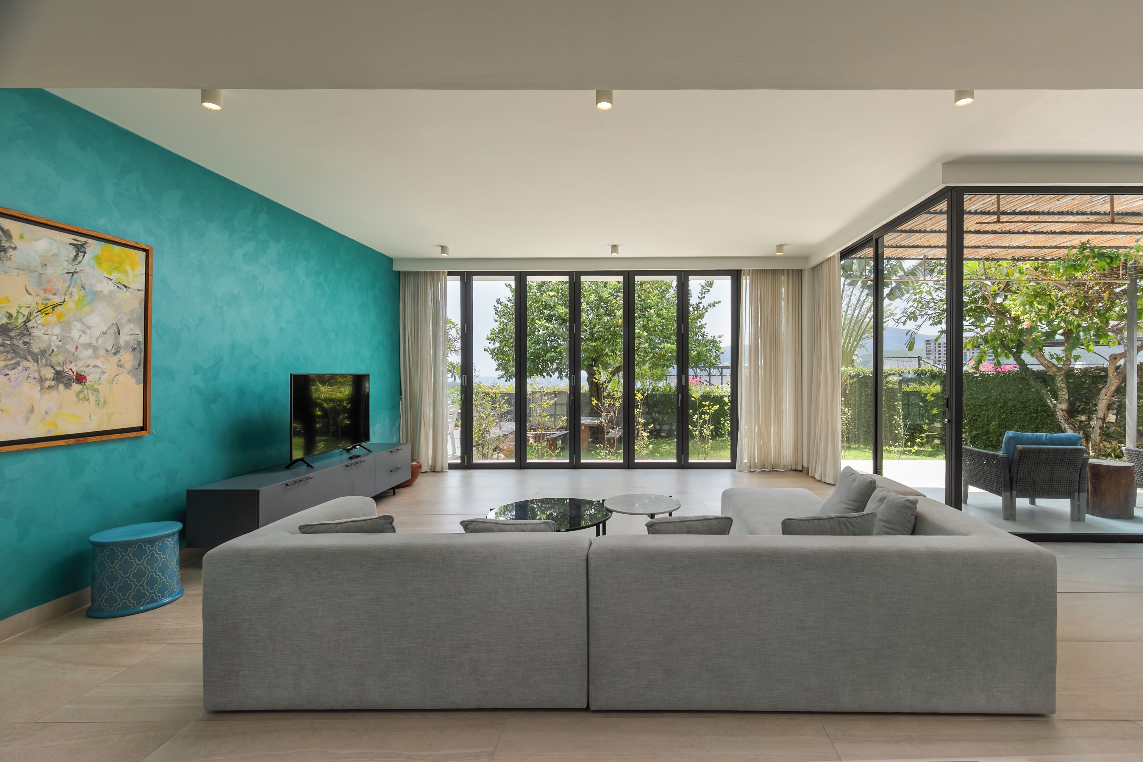 Uma sala de estar moderna com um amplo sofá modular cinza, uma televisão de tela plana e uma grande janela com vista para o exterior.