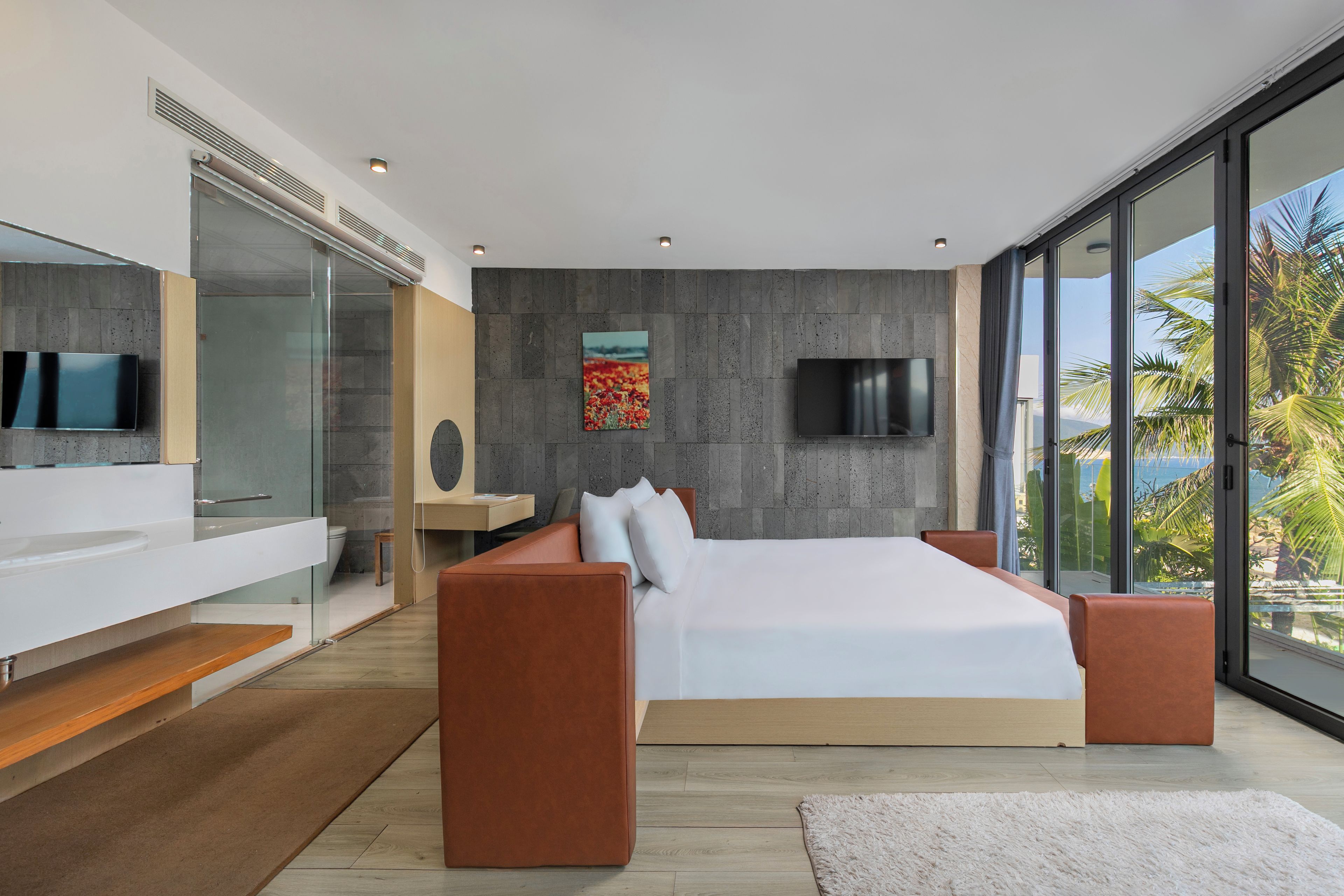 A modern bedroom with a large bed, a TV, and a view of palm trees.