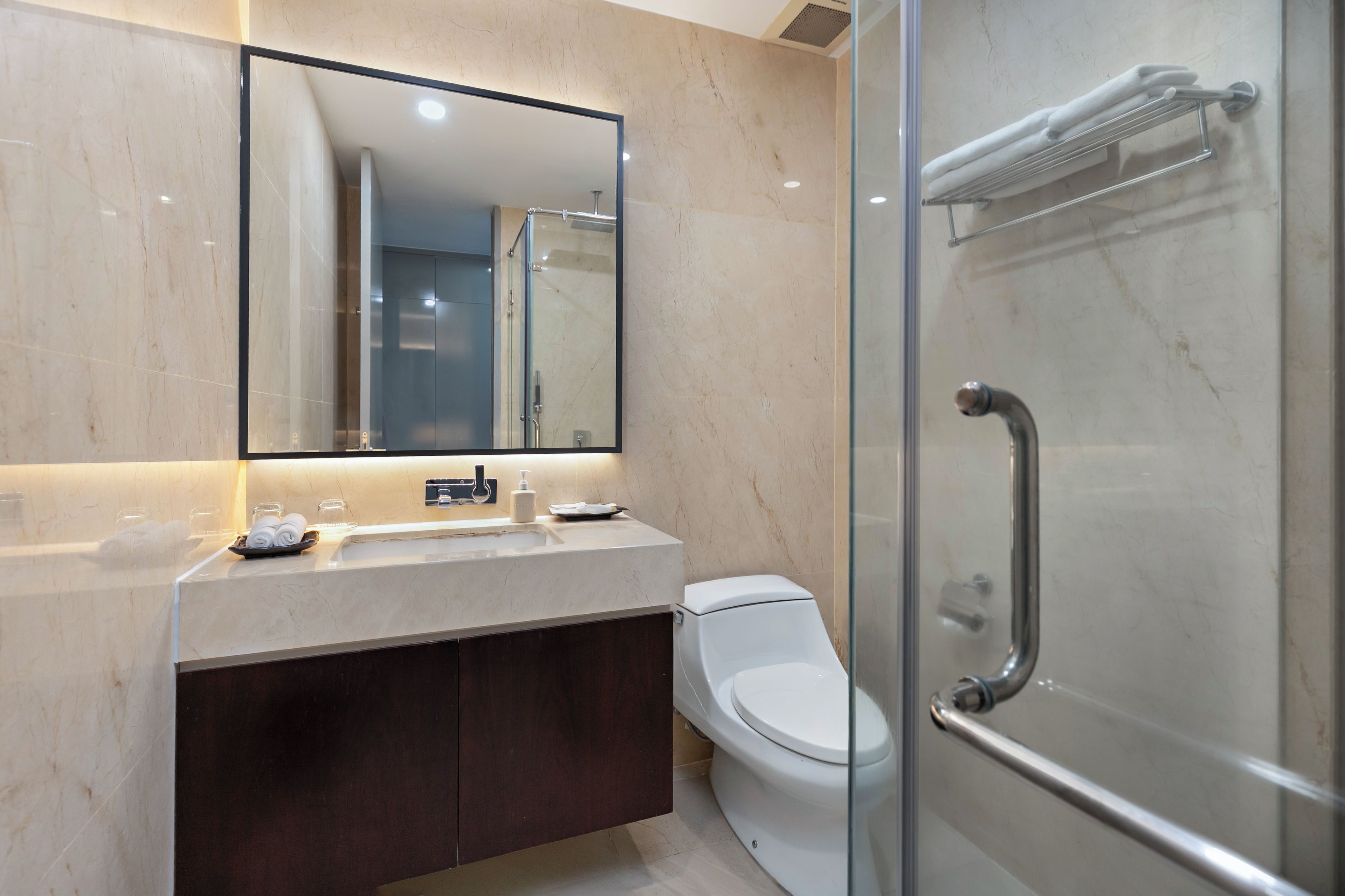Un baño moderno con cabina de ducha de vidrio, inodoro blanco y encimera de mármol con un espejo encima.