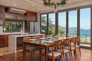 A modern kitchen with a large island, wooden cabinets, and a dining area with a view of the ocean.