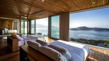 A modern hotel room with a large bed, wooden flooring, and a view of the sea.