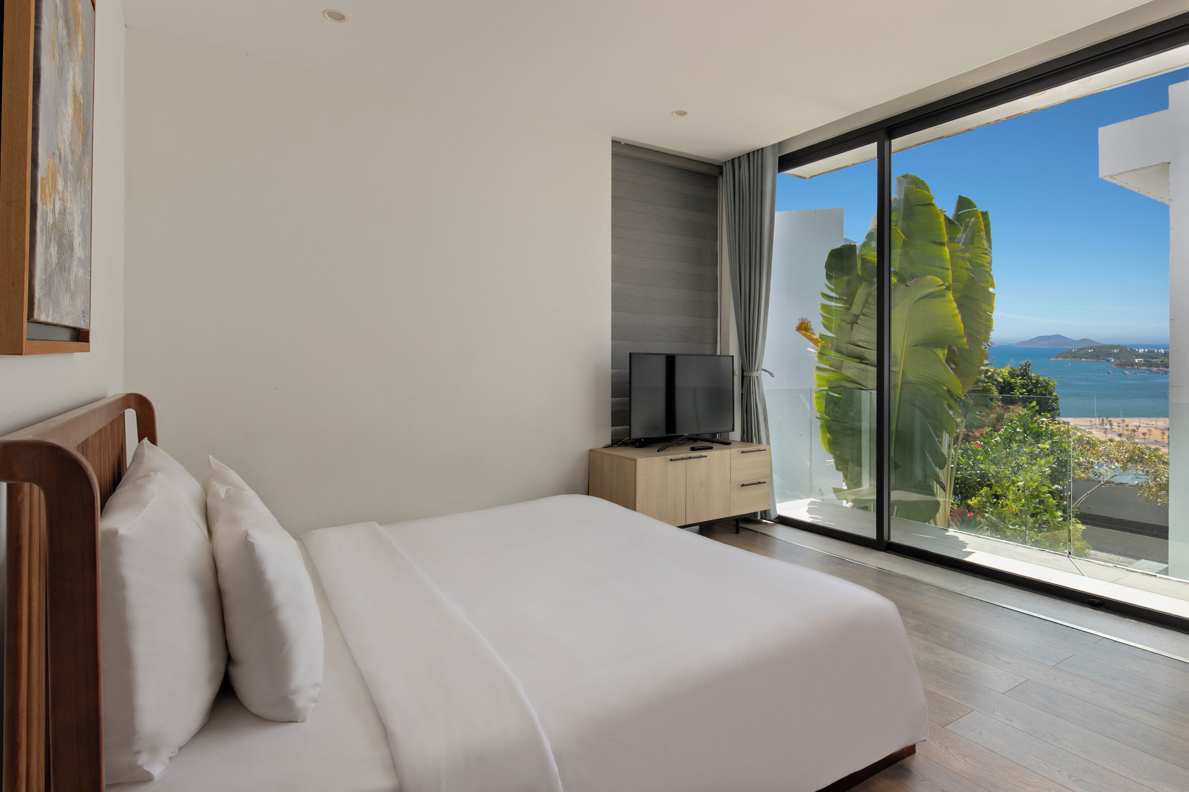 Ein Hotelzimmer mit einem gro ßen Bett, einem Fernseher auf einem Nachttisch aus Holz und Blick auf Meer und Berge.
