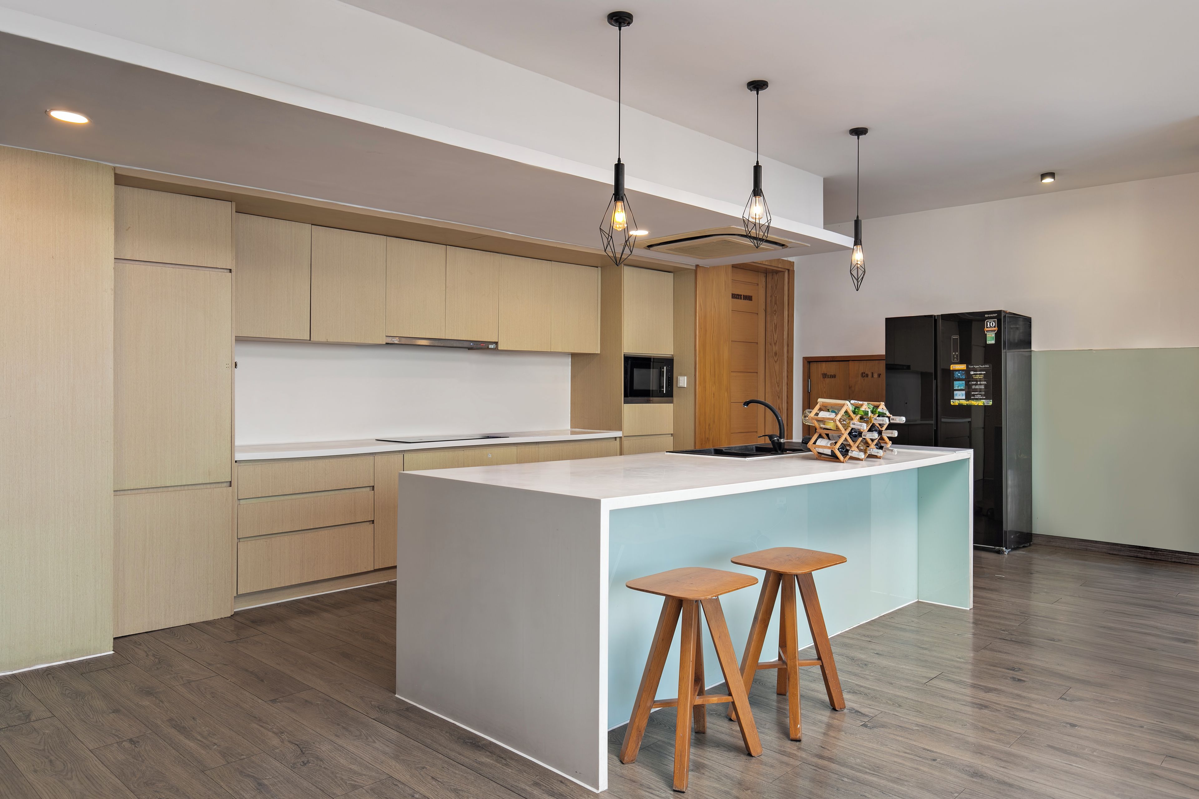 Eine moderne Küche mit Holzausstattung, einer zentralen Kochinsel mit Barhocker, einer eingebauten Mikrowelle und einem schwarzen Kühlschrank.