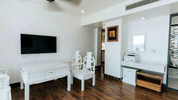 A room with a flat-screen TV mounted on the wall, a ceiling fan, a desk with a chair, and a printer on a counter.