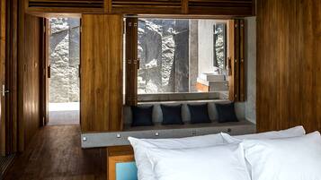 Un dormitorio moderno con techo de madera, una cama grande con ropa blanca, un banco con cojines y vistas a un paisaje nevado a través de amplios ventanales.