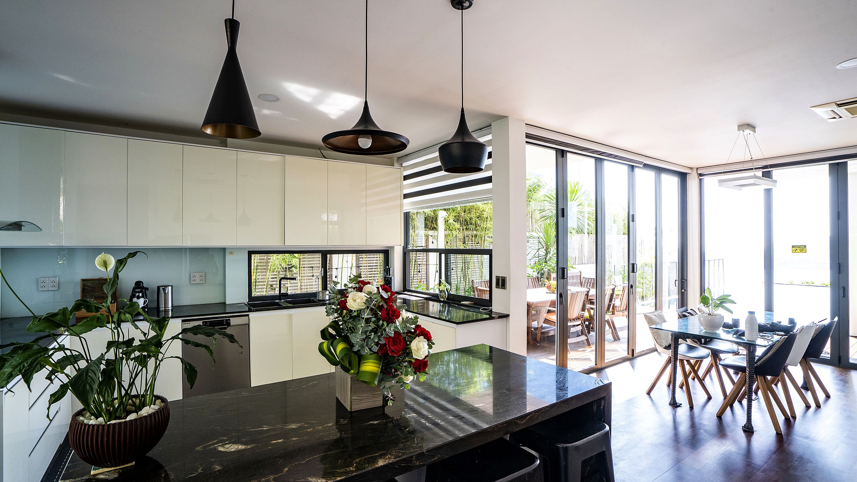 A modern kitchen with a central island, pendant lighting, and a view to an outdoor dining area.
