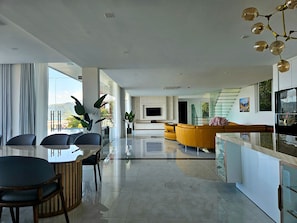 Una sala moderna con sofá, comedor con mesa y sillas, cocina con televisor y escalera.