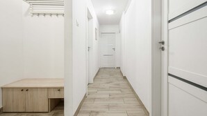 Um corredor estreito com um banco de madeira, paredes brancas e uma porta no final.